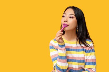 Güzel Asyalı kadın sarı arka plana ruj sürüyor.