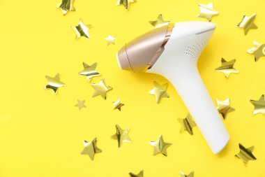 Sarı arka planda modern fotoepilatör ve altın yıldızlı kompozisyon