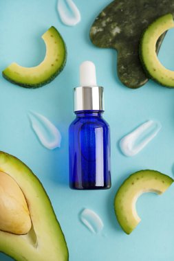 Taze kesilmiş avokado, krem örnekleri ve mavi arka planda bir şişe gerekli yağ içeren kompozisyon, yakın plan.