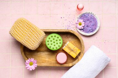 Banyo malzemeleriyle silikon kafa masajı fırçası, pembe arka planda deniz tuzu ve çiçekler.