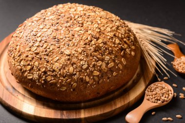 Tahta tahta tahta, taze ekmek, buğday dikenleri ve siyah arka planda kaşık tahıl.