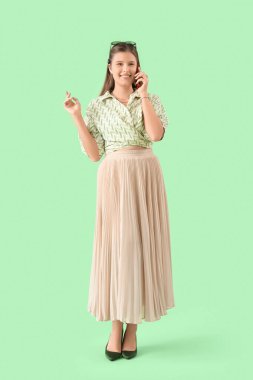 Gülümseyen genç kadın yeşil arka planda cep telefonuyla konuşuyor.