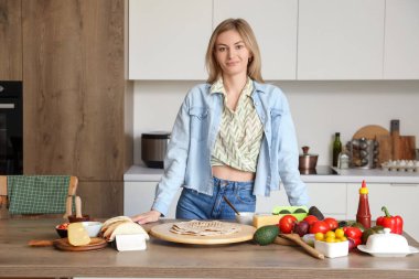 Mutfaktaki masada lezzetli tacolar yapan genç bir kadın.