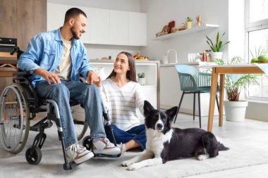 Tekerlekli sandalyedeki genç adam, karısı ve köpeği evde.
