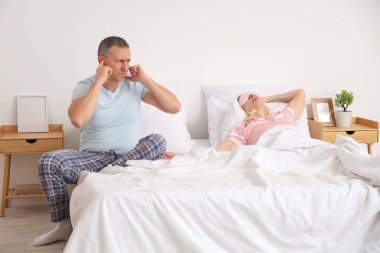 Karısının yatak odasında horlaması yüzünden sinirli, olgun bir adam kulaklarını kapatıyor.