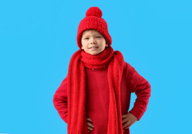 Sıcak kırmızı süveter, atkı ve mavi arka planda kış şapkası giyen yakışıklı bir çocuk.