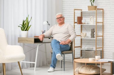 Oturma odasında sandalyede oturan yakışıklı son sınıf öğrencisi.