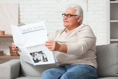 Yakışıklı son sınıf öğrencisi gazete okuyor ve oturma odasında kanepede oturuyor.