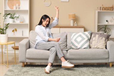 Evdeki kanepede oturan mutlu genç kadın.