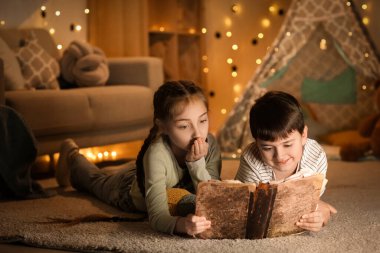 Tatlı çocuklar akşamları evde yerde macera kitabı okuyorlar.