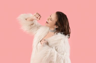 Pembe arka planda dans eden kürklü genç kadın.