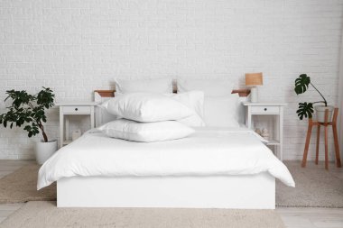 Beyaz battaniyeli rahat yatak ve şık yatak odasında bir yığın yumuşak yastık.