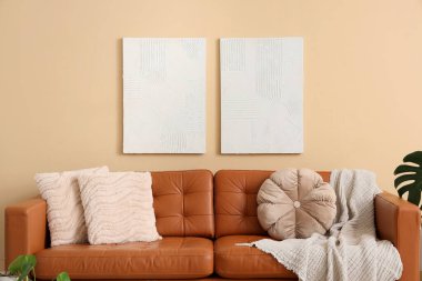 Oturma odasının içinde yastıklar ve ekoseli kahverengi deri kanepe, bej duvarın yanında.