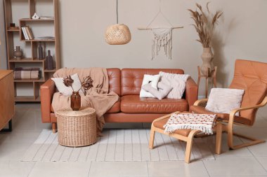 Rahat bir kanepe, ayak sehpası ve vazo içinde kurutulmuş çiçekler oturma odasının iç kısmında sepette.