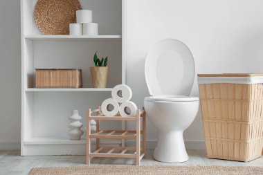 İçinde klozet, raf ünitesi ve sepeti olan ışık tuvaleti.