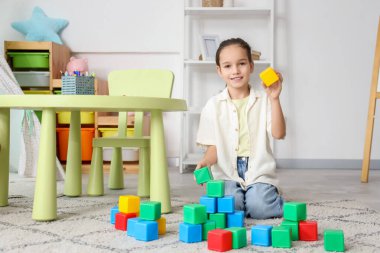 Evdeki halının üstünde küplerle oynayan tatlı bir kız.