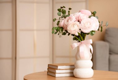 İçinde bir buket güzel ranunculus çiçekleri olan bir vazo ve şık oturma odasındaki sehpanın üzerinde kitaplar, yakın plan.