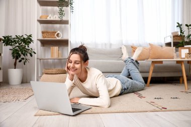 Evde dizüstü bilgisayarı olan güzel genç bir kadın dinleniyor.