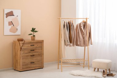 Sallanan giysiler, çekmeceler ve odada bej duvarın yanındaki puf.