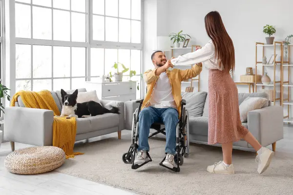Tekerlekli sandalyedeki genç adam ve evde dans eden karısı.