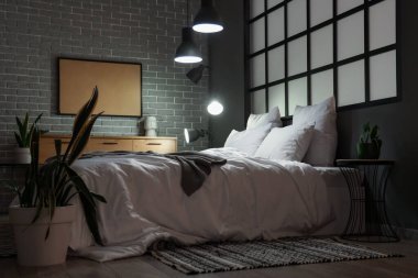 Geceleri rahat yatağı ve parlak lambaları olan modern yatak odasının içinde.