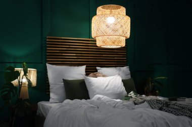 Geceleri modern yatak odasında buruşuk battaniyeli, parlak lambalı rahat bir yatak.