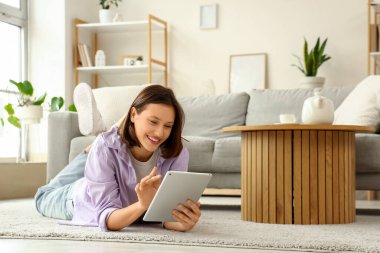 Evdeki halıda tablet bilgisayar kullanan genç bir kadın.