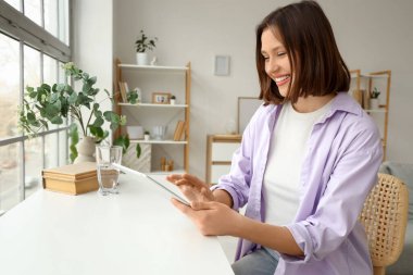 Masanın yanında tablet bilgisayar kullanan genç bir kadın.