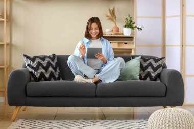 Evdeki koltukta modern tablet bilgisayar kullanan genç bir kadın.