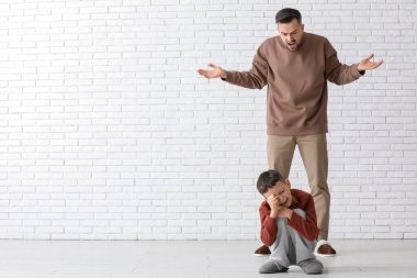 Kızgın baba ağlayan oğluna beyaz tuğla duvarın yanında bağırıyor.