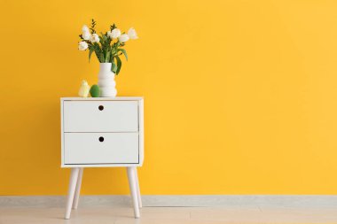 Vazo dolusu lale çiçeği, Paskalya yumurtası ve turuncu duvarın yanındaki komodinin üstünde civciv.