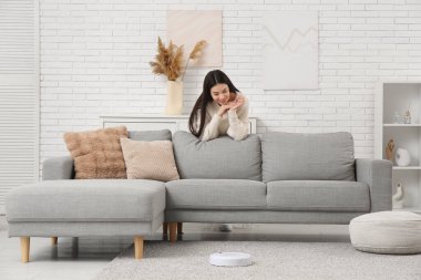 Evde elektrikli süpürgeyle kanepeye yaslanan genç bir kadın.