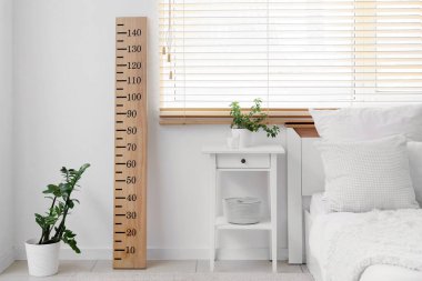 Yatak odasının içi komodinli, çiçekli ve pencere kenarındaki ahşap stadyumlu.