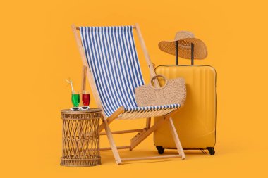 Hasır çantalı çizgili sandalye, bavul ve sarı arka planda kokteyl bardakları.