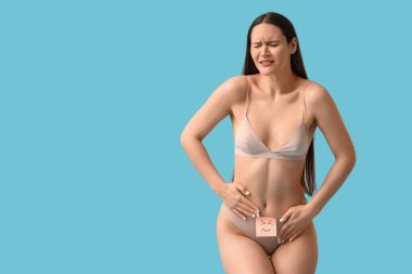 Mavi arka planda hüzünlü ifadeleri olan acı çeken genç bir kadın. Sistit kavramı