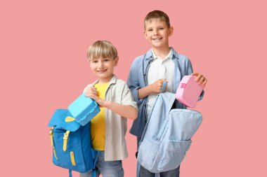 Küçük okul çocukları beslenme çantalarını pembe arka planda sırt çantalarına koyuyorlar.