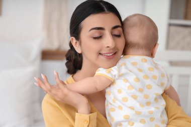 Güzel, genç, mutlu bir anne, küçük tatlı kızını evinde kucaklıyor.