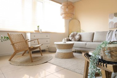 Oturma odasının içinde gri kanepe, koltuk ve rattan masa var.