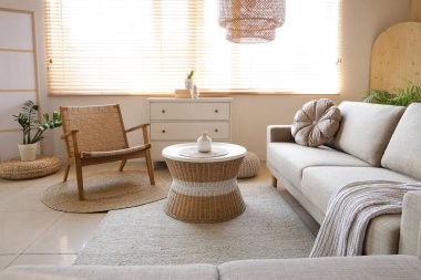 Oturma odasının içinde gri kanepe, koltuk ve rattan masa var.