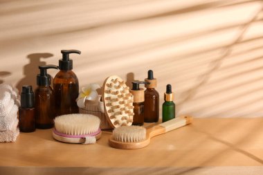 Farklı kozmetik ürünleri şişeleri, masaj fırçaları ve renkli duvarın yanındaki ahşap masa üzerindeki havlular.