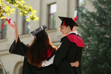 Mezuniyet gününde kucaklaşan diplomalı birkaç mutlu öğrenci.