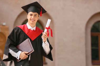 Mezuniyet gününde diploması ve kitabı olan mutlu bir erkek öğrenci.