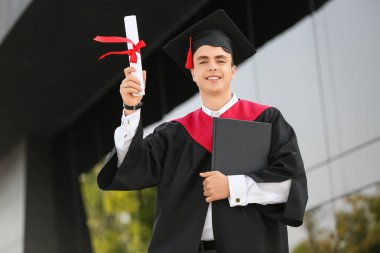 Üniversitenin yanında diploması ve kitabı olan erkek mezun.