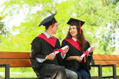 Dışarıda bankta oturan diplomalı bir çift mezun öğrenci.