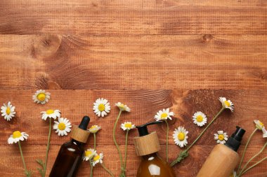 Ahşap arka planda kozmetik ürünleri ve papatya çiçekleri, yakın plan.