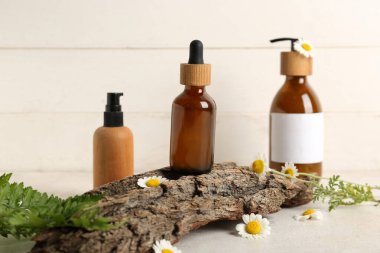 Beyaz grunge arka planda papatya çiçekleri, ağaç kabuğu ve kozmetik ürünleri şişeleri ile kompozisyon, yakın plan