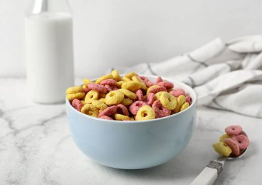 Hafif arka planda lezzetli mısır gevreği halkaları, kaşık ve süt dolu bir kase.