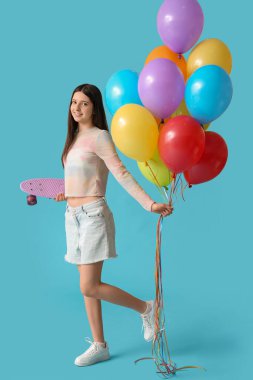 Mavi arka planda renkli balonları ve kaykayı olan güzel bir genç kız.