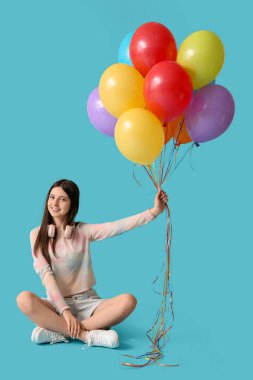 Mavi arka planda oturan renkli balonları ve kulaklıkları olan güzel bir genç kız.