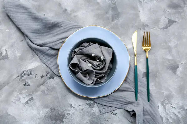 Altın çatal bıçak takımı ve gri arkaplanda çingene çiçekleri olan güzel bir masa.